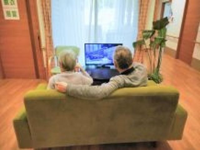 共有リビングの様子 日常風景 ソファでくつろぎながらテレビを楽しむ二人のご様子です。共有空間は温かみのあるインテリアで構成され、居心地の良い時間を提供します。