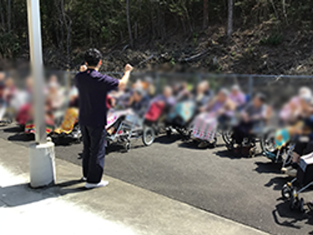 車椅子利用者と職員の様子 外観 屋外での活動に参加する皆さんが和やかに過ごしています。職員が丁寧にサポートしています。