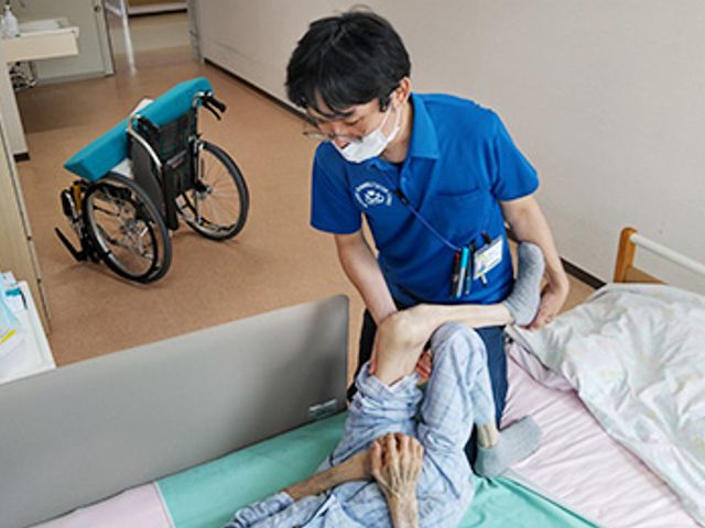 ベッドケア中の居室 居室 居室でのケア中で、介護職員が利用者の体勢を整えています。優しいサポートが魅力です。