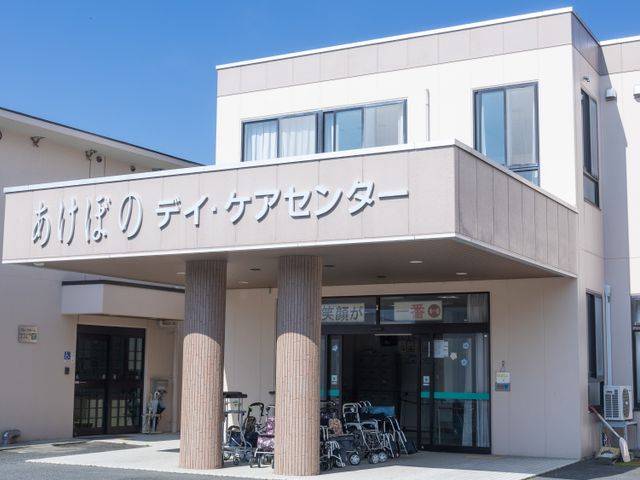 車椅子のある入口 エントランス 広々としたエントランスには、複数の車椅子が整然と配置されています。建物の外観がモダンで、青空の下で落ち着いた雰囲気です。