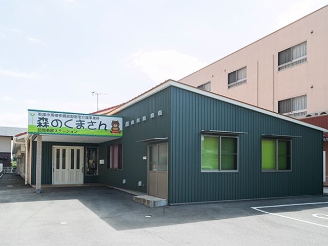 緑の壁の明るい建物 外観 緑色の壁が目を引く、明るく清潔感のある建物です。広々とした駐車スペースも整備されています。