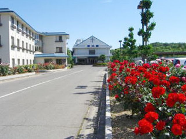 美しい花壇が並ぶ施設 外観 赤い花が咲く庭園沿いの道から見える施設の外観です。庭の手入れが行き届いています。