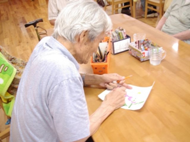 塗り絵を楽しむ様子 ラウンジ 明るい木製のテーブルで、入居者が楽しく塗り絵をしています。暖かな雰囲気が特徴の共有スペースです。
