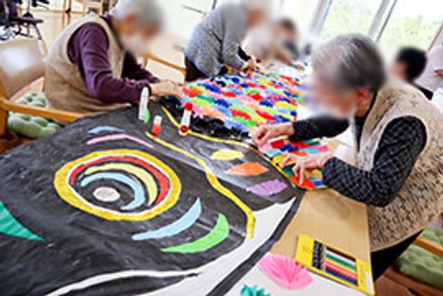 工作を楽しむ様子のラウンジ ラウンジ 明るい空間で、入居者の方々が楽しく工作をしています。和やかな交流が見られる場所です。