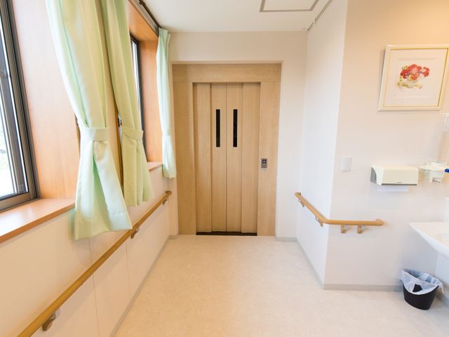 清潔感ある居室の一角 エレベーターホール 手すりが付いた通路と洗面台があり、日々の生活に配慮された設計です。明るくゆったりした空間が皆様をお迎えします。