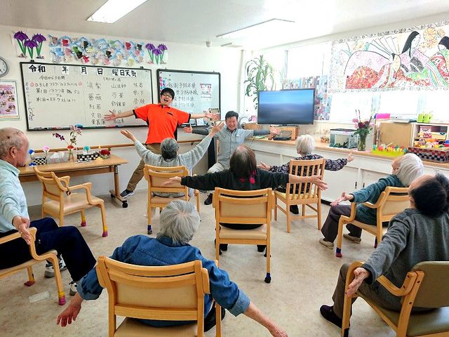 体操する人々の居室 居室 自然光に包まれた広々とした空間で、入居者の方々が集まって体操を楽しんでいます。体を動かしながら健康維持が図れます。
