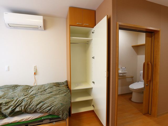 居室のベッドとトイレ 居室 清潔感のある居室内には、必要な備品が整っており、快適な生活をサポートします。トイレも部屋に隣接しており、利便性が考慮されています。