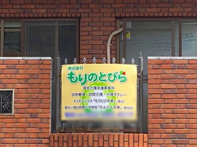 屋外の看板 看板 レンガ壁に設置された看板には、介護事業の詳細情報が記載されています。施設の外観から確認できます。