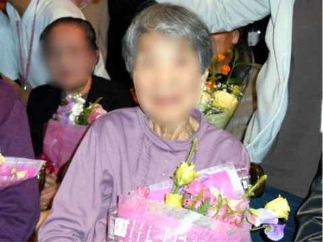 お祝いする人々の集い イベント 心温まる光景です。手に花束を持ち笑顔の方が、周りの人に囲まれて特別な時間を過ごしています。