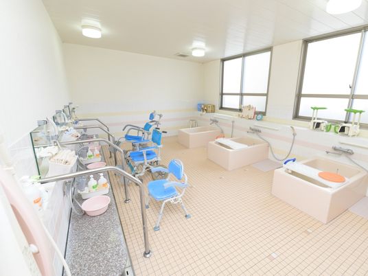 個浴槽を3台備えた広い浴室で、洗い場も複数ある。洗い場にシャワーチェアや浴室用の車椅子が置かれている。
