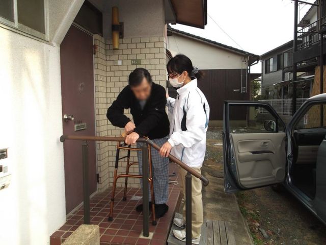 外でのサポートの様子 外観 車のそばで支援者が利用者をサポートしています。介護における温かな瞬間です。