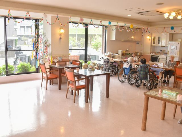 明るいダイニングの様子 食堂1 窓辺のダイニングで利用者様が集い、心地よい光の中で会話を楽しんでいます。ゆとりある空間は働く環境としても魅力でしょう。