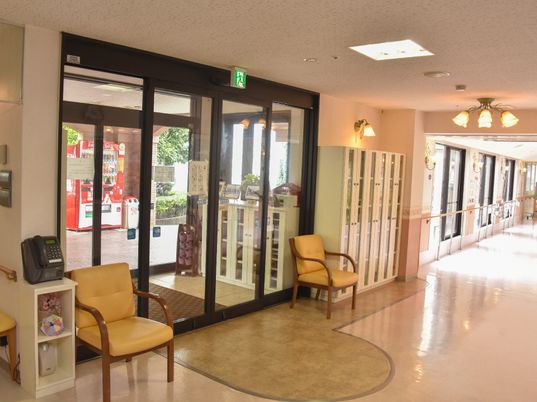 施設玄関の両開きの自動ドアは、ストレッチャーや車椅子が楽に通行できる幅がある。補助椅子や公衆電話、自販機の備付もあり便利。