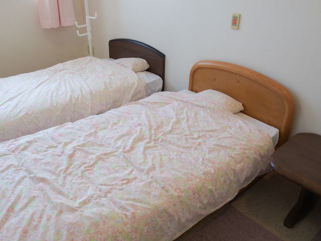 快適な居室のベッド 部屋 落ち着いた色合いの居室で、ゆったりとしたベッドが二つ備え付けられています。安らぎの空間をご提供します。