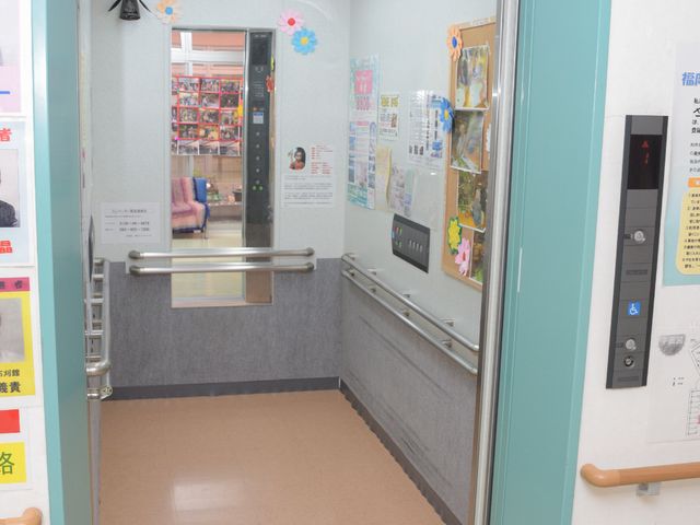施設のエレベーター入口 エレベーター ゆったりとしたエレベーターは、バリアフリー構造で安心です。扉に貼られた掲示物も彩りを添えています。