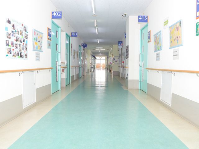 明るく広い施設の廊下 廊下 手すりが取り付けられた清潔感のある廊下です。壁には、掲示物やアートが飾られ、温かみのある雰囲気を醸し出しています。