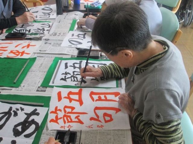 書道を楽しむ様子 レクリエーション 様々な活動で心を豊かに。筆を持つ手が集中して書を揮っており、創作の時間を大切にしています。