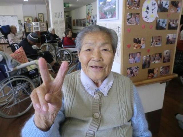 明るい笑顔の高齢者 入居者様 和気あいあいとした多目的室で、入居者同士がコミュニケーションをとっています。手を挙げてポーズを取る元気な様子が、明るい雰囲気を伝えています。