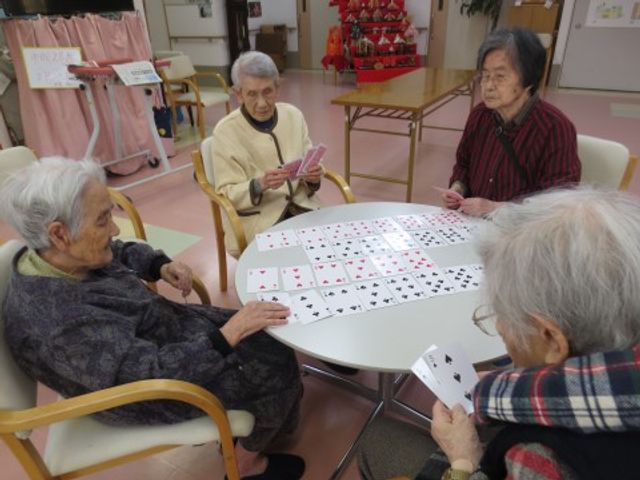 高齢者のカードゲーム 入居者様 温かな雰囲気の多目的スペースで、楽しそうにカードゲームをされる方々。こちらでリフレッシュの時間を過ごせます。