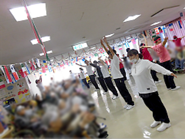 運動する様子の部屋内 多目的室 スタッフと利用者が一緒に運動を楽しんでいます。開放的で交流しやすい雰囲気があります。