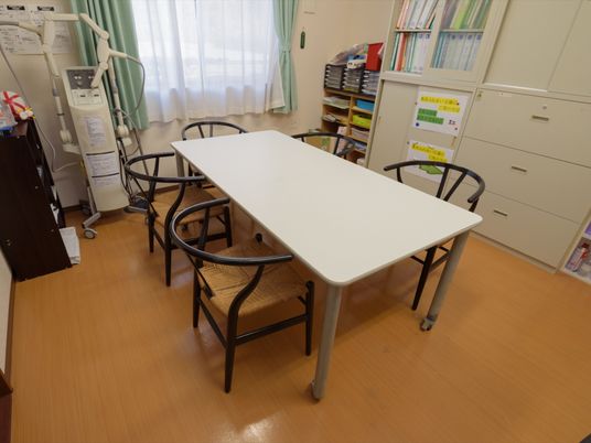 明るい清潔感のあるスタッフルームには、テーブルとイスが５脚完備されている。書棚には入居者様のデータファイルが収納されている。