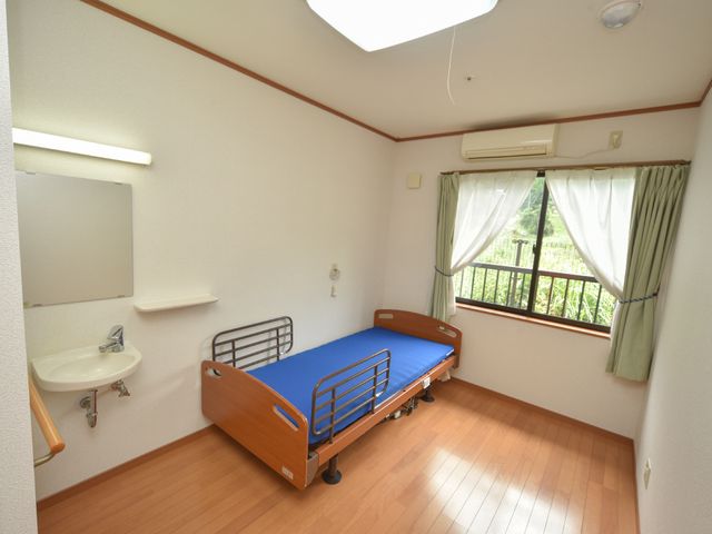 清潔な居室の一角 居室 ベッド横の窓から自然光が差し込み、木々が見える落ち着いた空間です。