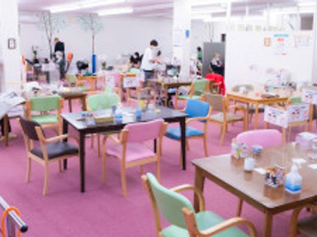 ゆったり共有スペース 多目的室 やすらぎのひとときを過ごせる、明るく広々とした多目的室です。ソフトな色調の椅子に腰掛け、穏やかに過ごす方々の姿が見受けられます。