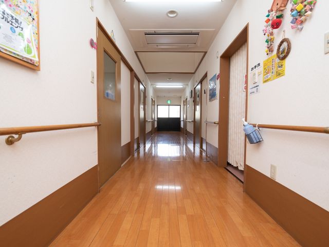 清潔感ある廊下 通路 手すりが設けられた明るい通路を備え、安心して歩行できる環境が整っています。壁には温かみのある工芸品も飾られ、心地よい雰囲気を演出しています。