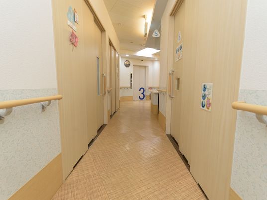 廊下の両サイドには、居室やトイレが設けられている。突き当りには、エレベーターが設置されている。壁に手すりが取りつけられている。