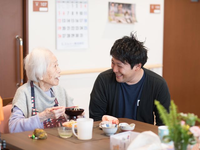 笑顔で会話する二人 笑顔あふれる食事の時間を、ご利用者とスタッフが一緒に楽しんでいます。毎日の食事が、温かいふれあいの場となっています。