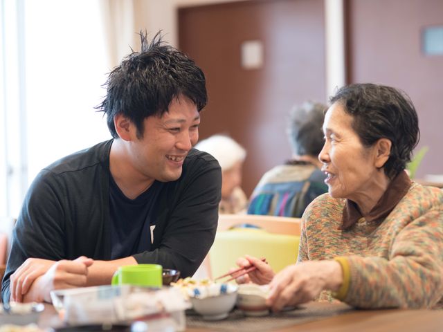 笑顔で会話する二人 心温まる会話が弾む食堂の一幕です。手を添えながら、優しくサポートしている様子が伺えます。