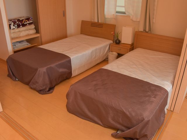 清潔感のある居室 二人部屋 床から天井までの明るい色合いで統一された落ち着いた居室です。二つのベッドと充分な収納スペースが確保されており、快適な生活が送れるよう工夫されています。