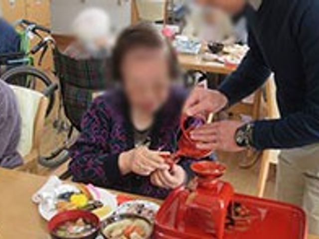 食事の配膳を手伝う場面 ダイニングルーム 明るい空間で、スタッフが親身になって食事のサポートをしています。交流がしやすい環境です。