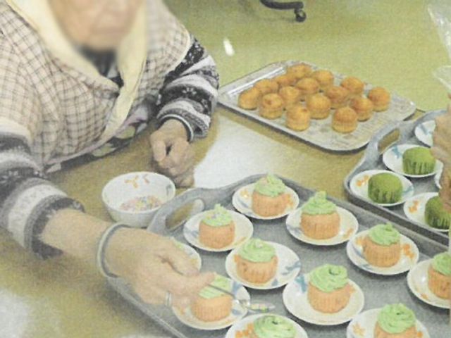 カップケーキを並べる場面 食堂 施設内の協働作業で、利用者同士がカップケーキを用意しています。和やかな雰囲気が広がります。