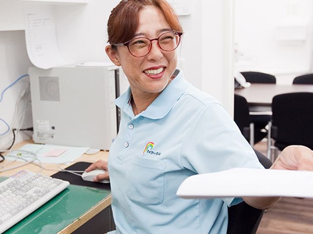 書類を手渡すスタッフ スタッフイメージ スタッフが親しみやすい笑顔で対応しています。介護施設での仕事に興味のある方に最適な環境です。