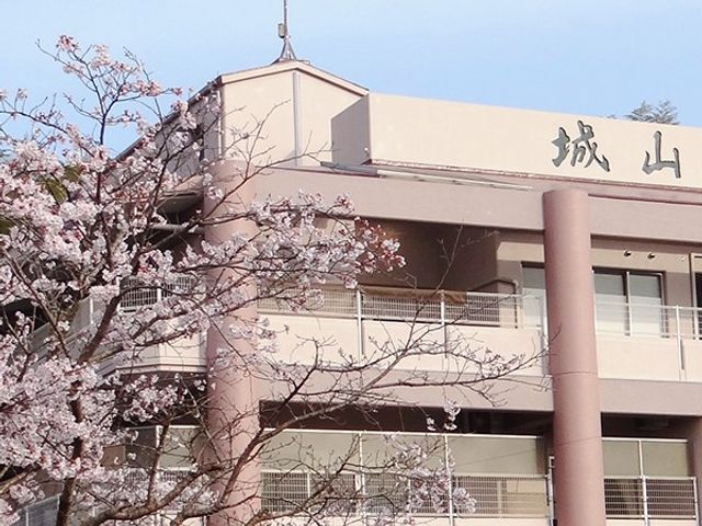 桜と建物の外観 外観   桜の枝が手前に広がり、建物のやわらかな色合いが穏やかな印象です。明るい雰囲気で、働く場としての景色が伝わります。