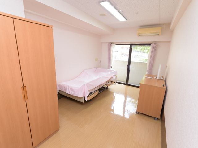 居室のベッドと窓 居室 ゆったりとした個室で、明るい光が差し込む窓からは外の景色を見ることができます。快適な生活空間が整っており、プライバシーも守られています。