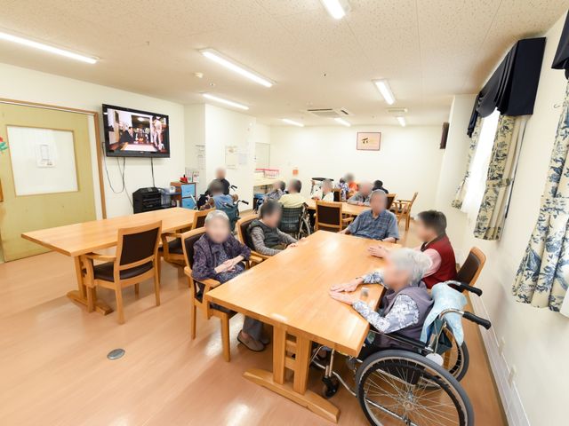 共有スペースの様子 共有スペース 明るい食堂では、利用者がテレビを視聴しながらくつろいでおり、温かい雰囲気が漂っています。テーブルには車いす使用の方もゆったりと対面できる十分なスペースがあります。