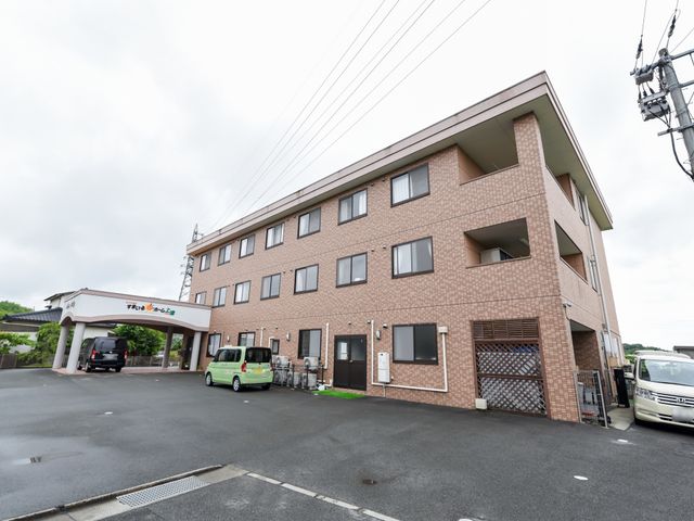 茶色の建物の外観 外観 広々とした敷地に建つ明るい色調の建物です。ゆったりとしたアプローチが印象的で、来訪者を温かく迎えてくれる雰囲気があります。