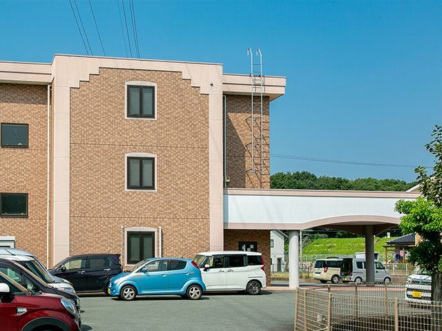 建物外観と駐車場 外観   落ち着いた色合いの建物外観と、複数台が停められる駐車場が見えます。送迎や来訪時の動線をイメージしやすい外まわりです。