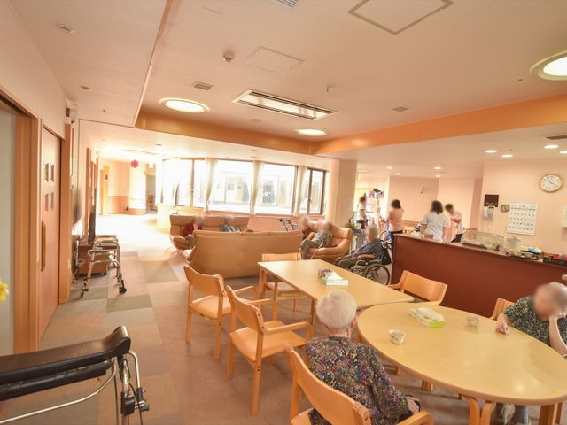 和やかな食堂の様子 食堂 温かみのある色合いの食堂です。複数の利用者がくつろぎながら、食事や会話を楽しんでいる様子が伺えます。