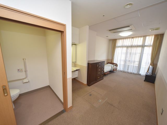 明るい居室の内観 居室 ゆとりを持った居室では、大きな窓から自然光がたっぷりと入り、リラックスした時間を過ごせます。清潔感のあふれる空間が、働く環境の一端を示しています。