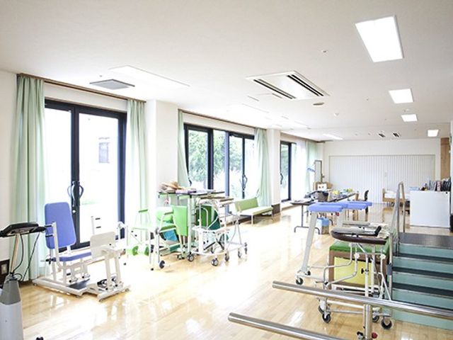 明るい機能訓練室 機能訓練室 広々とした機能訓練室で、明るい日差しが差し込む中、様々なリハビリ機器が整備されております。安心して身体を動かすことができる空間をご用意しています。