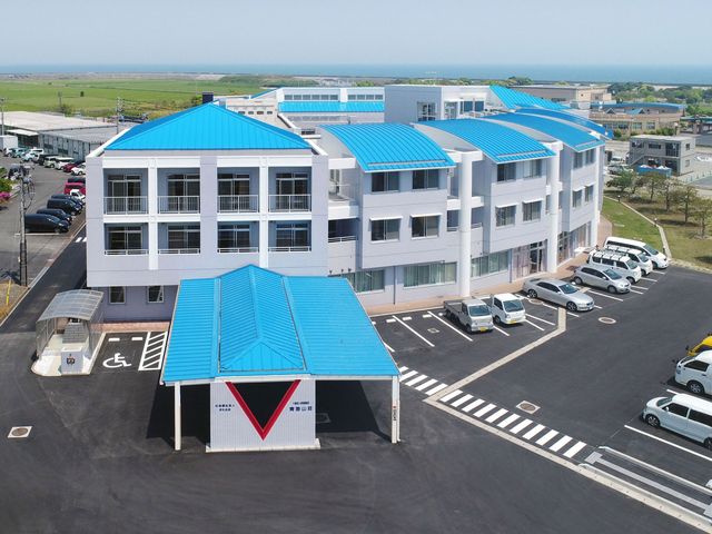 白い建物と駐車場 外観 広々とした駐車スペースのある建物です。青い屋根が爽やかさを感じさせます。