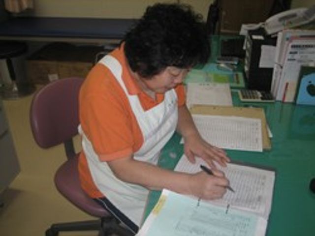 書類に記入するスタッフ スタッフイメージ スタッフが丁寧に書類を確認している様子です。細やかな業務が求められる環境です。