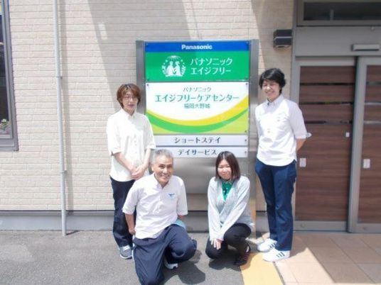 スタッフが看板前に並ぶ外観  