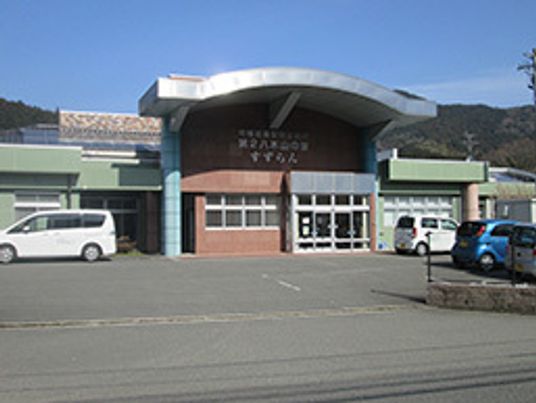 玄関先には大きな屋根が付き、駐車場も広い。周辺には緑の濃い山々がある。