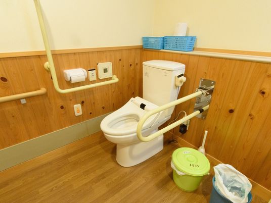 木のぬくもりが感じられる広々としたトイレ。壁には、ナースコールや操作パネル、手すりが設置されている。