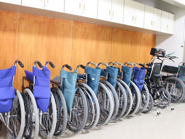 車椅子が並ぶ廊下 廊下   複数の車椅子が整然と並んでおり、必要な方がすぐ使える環境です。壁面収納のあるすっきりした廊下で、動線を確保しやすそうです。