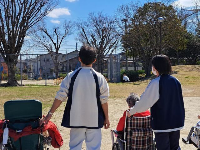 外を歩くスタッフと利用者 中庭 ゆったりとした時間が流れる外の散歩風景です。スタッフの優しい手引きで安全に歩行をサポートしています。